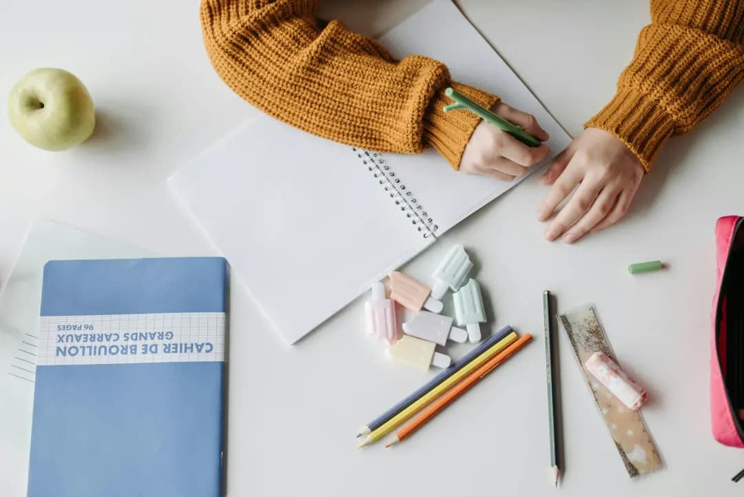 Enfant écrivant sur un cahier, entouré de crayons et d'un cahier de brouillon
